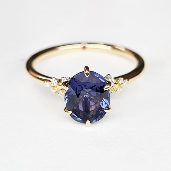 Blue purple oval sapphire in six claw prong setting with diamond cluster engagement ring