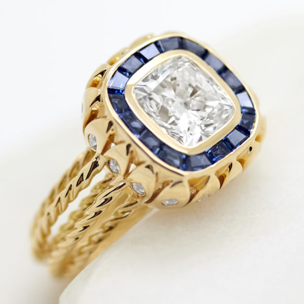 cushion cut diamond with custom cut blue sapphire halo and rope band in yellow gold
