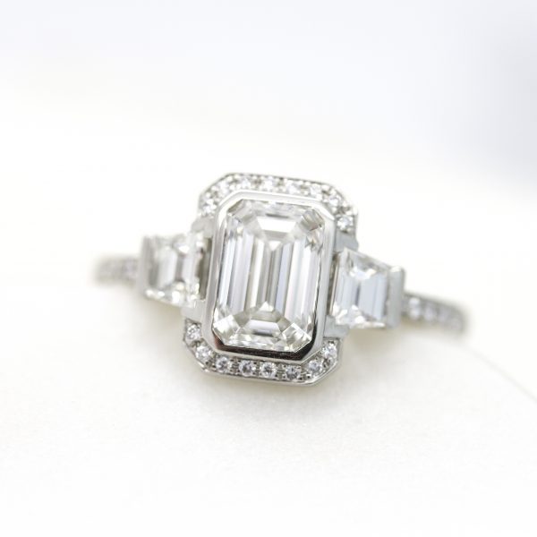 emerald cut diamond with step cut trapezoids in trilogy engagement ring