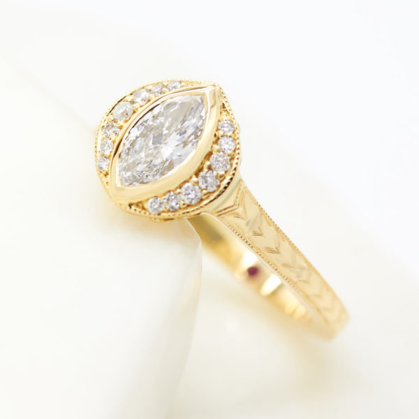 Vintage marquise bezel set diamond engagement ring with a round diamond semi halo and an engraved band with engraving and milgrain