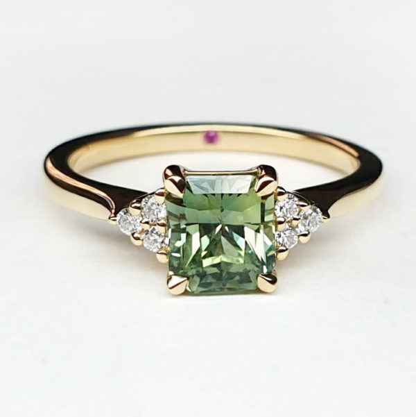 Radiant cut green sapphire with round diamond accent stones, set in yellow gold