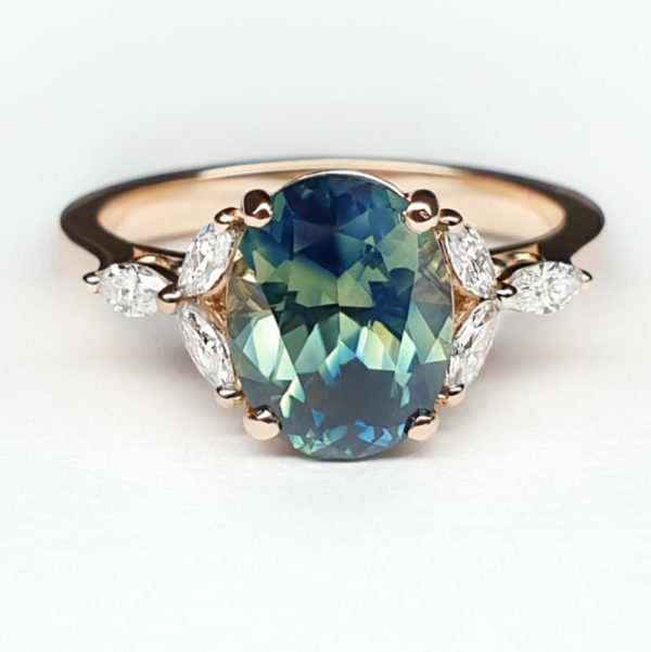 Teal bi-colour oval sapphire set in yellow gold with marquise accent diamonds