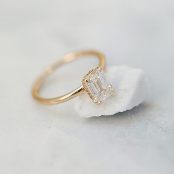 An emerald cut diamond with a hidden halo, on a yellow gold band